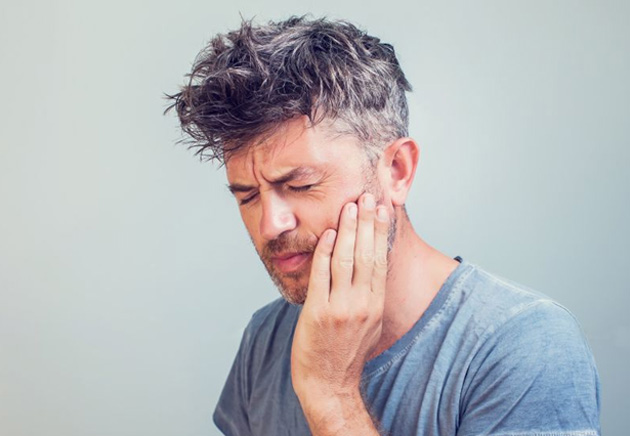 Man grimacing in pain, touching the side of his face
