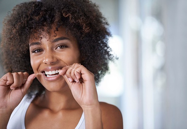 woman smiling while flossing her dental implants in Pittsburgh 