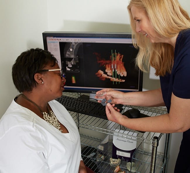 Dentist and patient looking at models of teeth and computer screen showing dental x rays