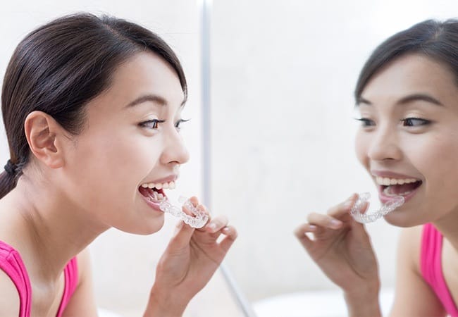 Woman looking in mirror as she places invisalign tray
