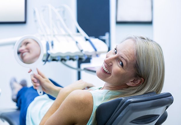 Smiling woman holding mirror in dental chair