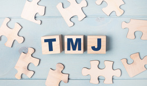 Blocks spelling out “TMJ” surrounded by puzzle pieces