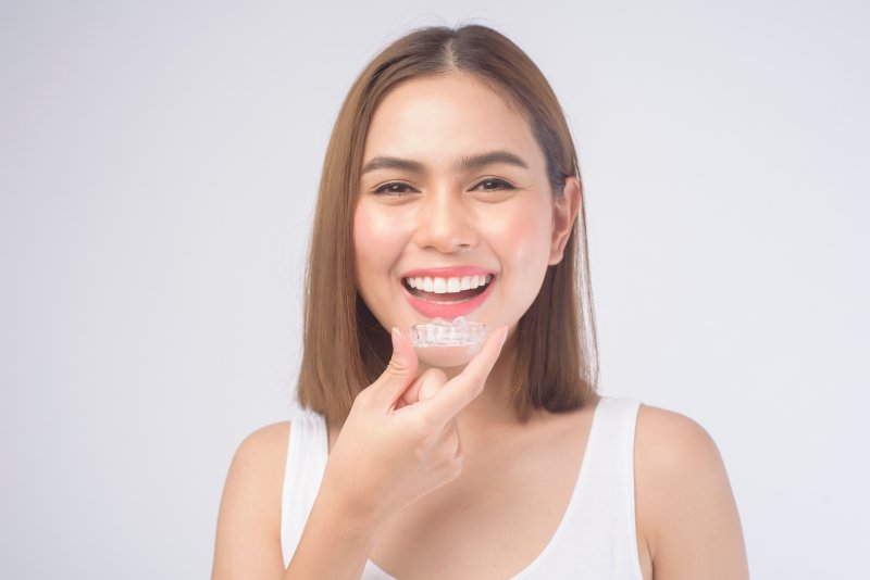 Woman smiling holding clear aligner to her teeth