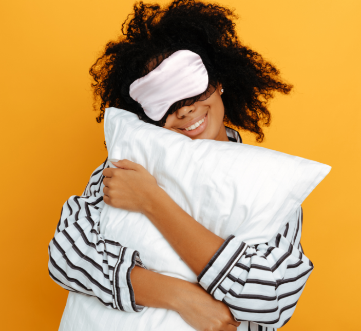 Woman with sleep mask in pajamas hugging pillow
